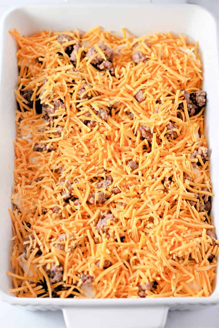 Cheddar cheese on top of sausage and biscuits in a casserole dish